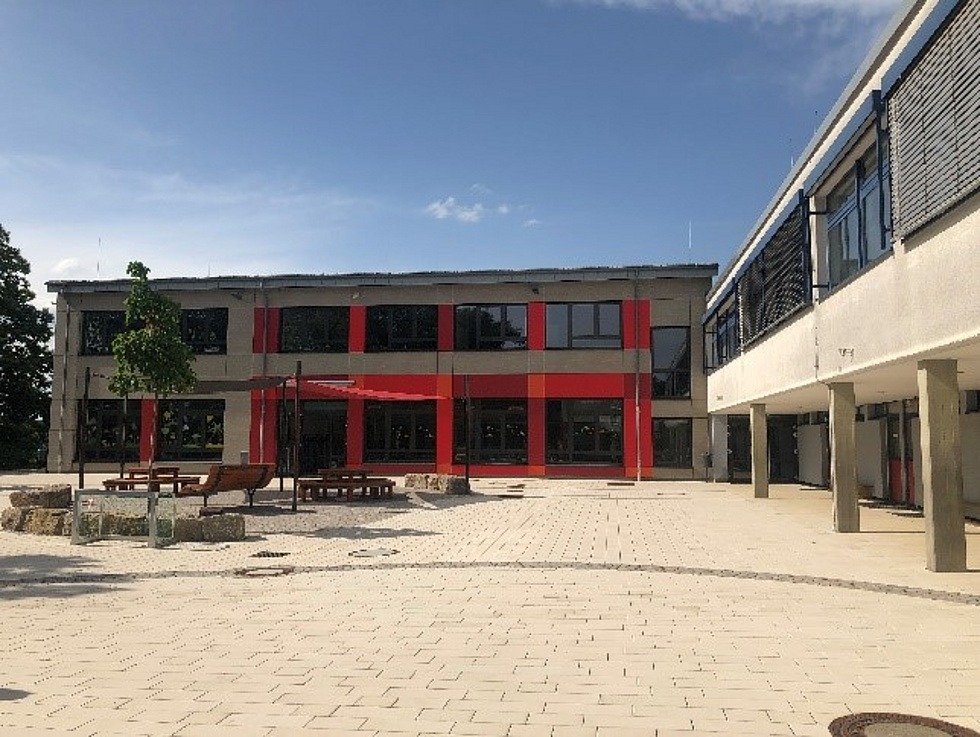 Schulgebäude, davor Schulhof mit Klettergerüst