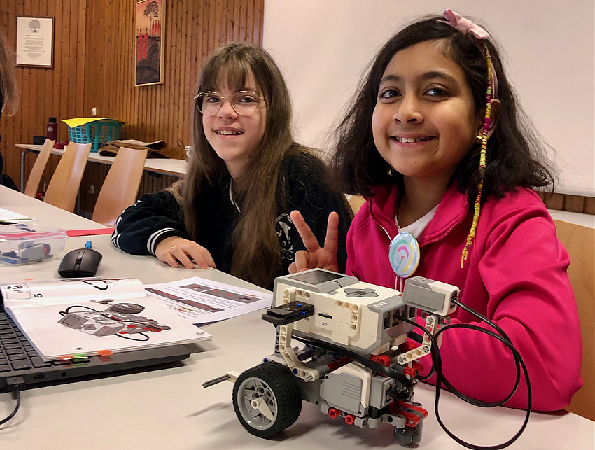 Zwei Mädchen sitzen an einem Tisch. Sie haben einen kleinen Roboter gebaut.