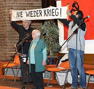 Joram Bejarano, Esther Bejarano, Kutlu Yurtseven halten ein Plakat in die Höhe: Nie wieder Krieg!