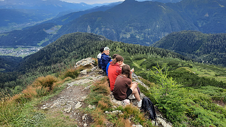 Jugendliche sitzen auf Berggipfel und blicken ins Tal